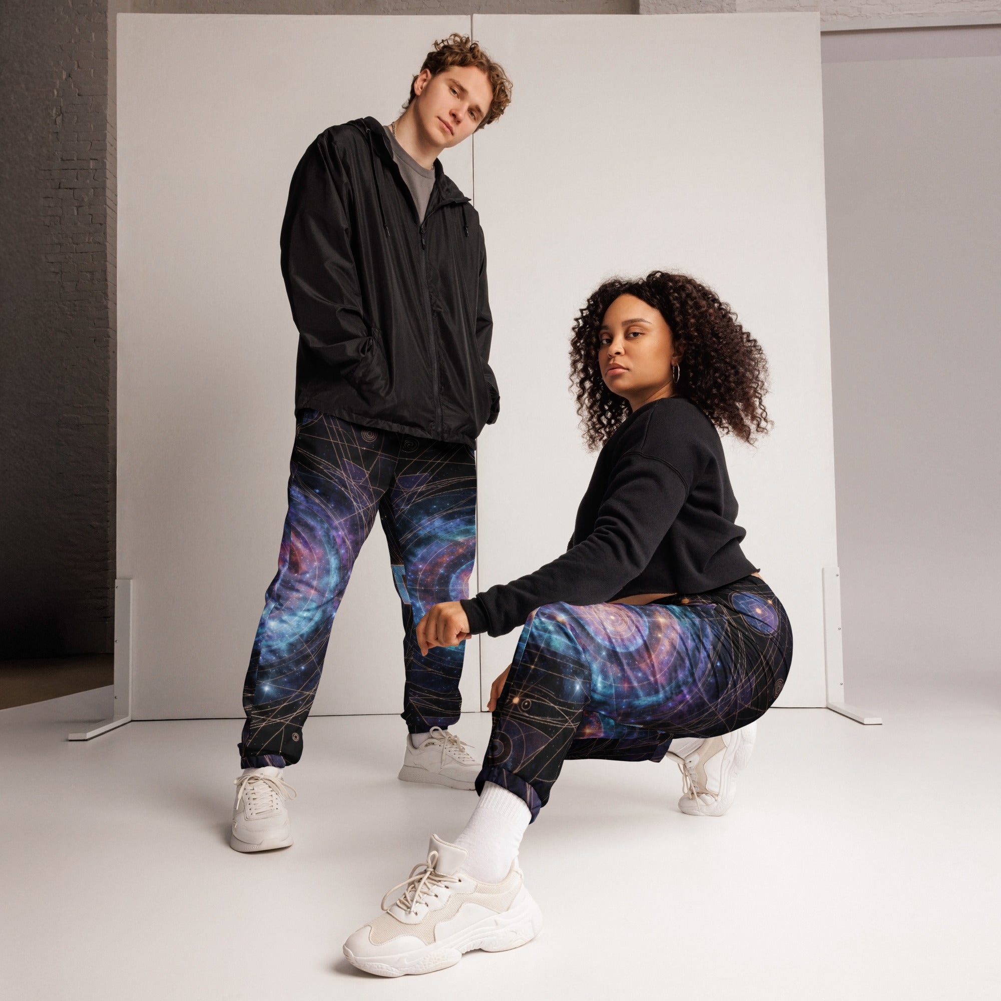 Couple wearing Galaxy Sacred Geometry Unisex Track Pants in cosmic mandala pattern, full lifestyle shot in studio